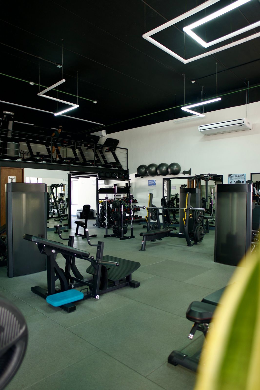 Piso de entrenamiento con máquinas y área de cardio arriba